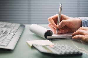 photo of a keyboard, calculator, and a person writing notes